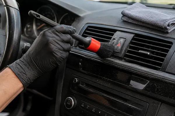 Detailed cleaning of pollen and dust from car air vents during interior detailing.